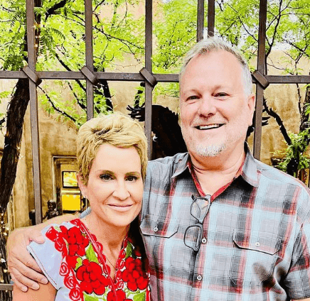 Smiling couple posing in front of a wrought iron fence with trees in the background.