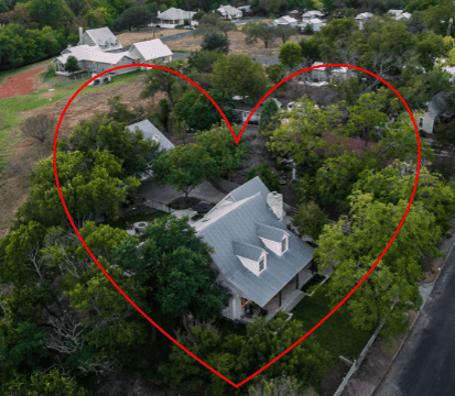 Aerial view of houses surrounded by trees with a red heart outline highlighting one house.