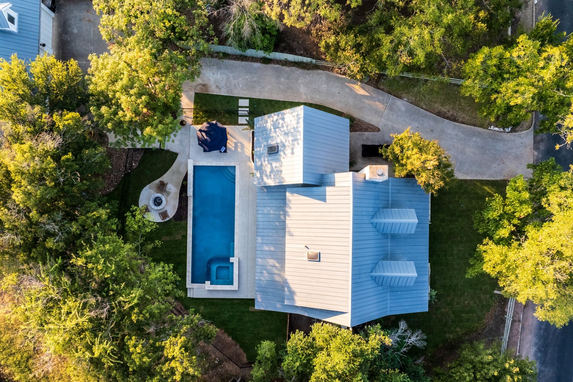 Aerial view of a house with a large pool, surrounded by trees and a landscaped yard.